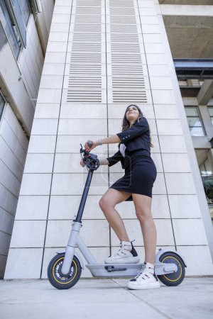 Téléchargez les photos : Gestionnaire féminine avec son scooter dans un environnement urbain moderne - en image libre de droit