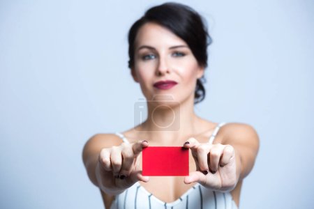 Téléchargez les photos : Femme blanche aux cheveux noirs vêtue d'une combinaison à rayures blanches pointe vers un carton rouge, isolée sur fond blanc - en image libre de droit