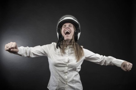 Photo for Blonde girl with protective motorcycle helmet simulates the gesture of acceleration on a motorcycle, isolated on a black background - Royalty Free Image