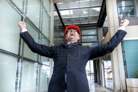Téléchargez les photos : Ingénieur avec casque rouge habillé en costume d'affaires dans un cadre urbain moderne - en image libre de droit