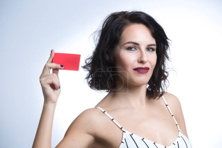 Téléchargez les photos : Femme blanche aux cheveux noirs vêtue d'une combinaison à rayures blanches pointe vers un carton rouge, isolée sur fond blanc - en image libre de droit
