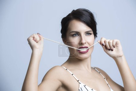 Photo for White woman with black hair dressed in a white striped jumpsuit, plays with the pearls of a necklace, isolated on white background - Royalty Free Image