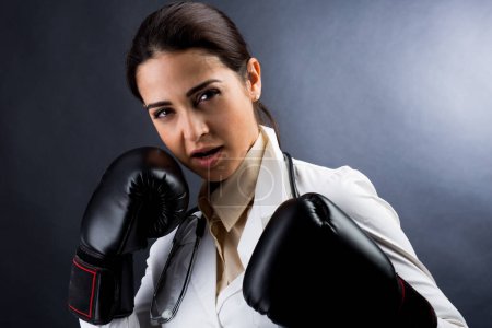 Photo for Female doctor in white coat and boxing gloves Has the expression of someone who doesn't want to give up, isolated on gray background - Royalty Free Image