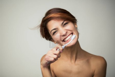 Foto de Hermosa chica con el pelo corto cepilla sus dientes con un cepillo de dientes, aislado sobre fondo claro - Imagen libre de derechos