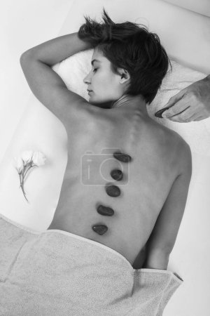 Téléchargez les photos : Femme aux cheveux frisés se détend sur le lit d'un spa couché sur son ventre tourné par le haut avec le dos au premier plan, noir et blanc - en image libre de droit