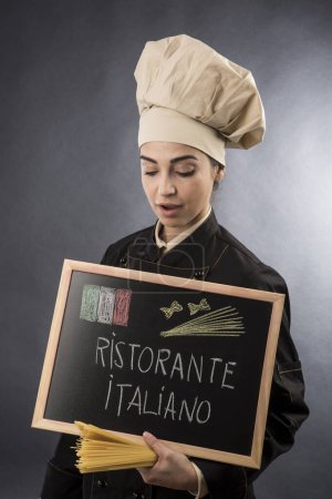 Téléchargez les photos : Femme cuisinière italienne tient un tableau avec "Restaurant italien" écrit dessus, isolé sur fond gris - en image libre de droit