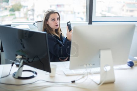 Foto de Rubia trabajadora de oficina sentada en la silla de trabajo cerca de su escritorio se ve con expresión seria - Imagen libre de derechos