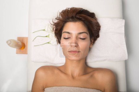 Téléchargez les photos : Portrait d'une fille détendue allongée sur un lit de spa avec une serviette enroulée autour de son buste - en image libre de droit