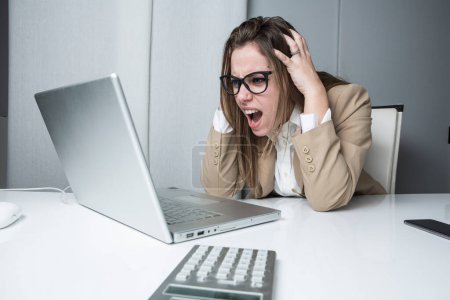 Foto de Gerente mujer en chaqueta y camisa se desesperó y trae sus manos a la cabeza sentado delante de su computadora portátil - Imagen libre de derechos