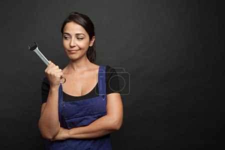 Téléchargez les photos : Belle fille avec des outils de travail ouvrier à la main et salopettes bleues gurada curieusement, isolé sur fond noir - en image libre de droit