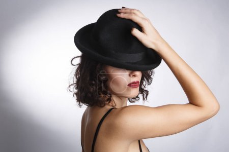 Téléchargez les photos : Belle brune dans une robe noire et chapeau noir posant isolé sur un fond blanc. - en image libre de droit