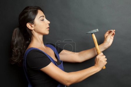 Photo for White girl with black hair beats a nail with a hammer, isolated on a black background - Royalty Free Image