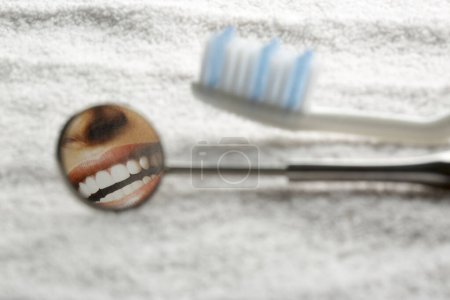 Zahnbürste und Zahnspiegel auf einem hölzernen Hintergrund mit einer Reflexion der menschlichen Zahnreihe