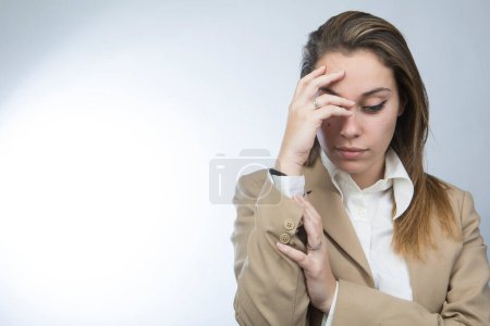 Photo for Blonde female manager in beige jacket brings hand to forehead and looks down with depressed expression, isolated over white background - Royalty Free Image