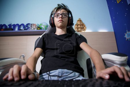 Téléchargez les photos : Adolescent avec écouteurs, commandes et claviers joue avec des jeux électroniques dans sa station d'origine - en image libre de droit