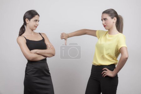 Photo for Two girls, one brunette and the other blonde are in disagreement and one of them makes the negative sign with the hands to the other, isolated on gray background - Royalty Free Image