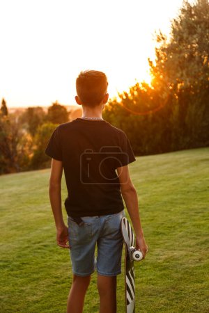 Photo for Boy from behind with his skateboard during sunset - Royalty Free Image