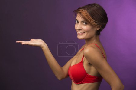 Foto de Chica con traje de baño rojo muestra su mano como si ella está sosteniendo algo, aislado sobre fondo gris - Imagen libre de derechos