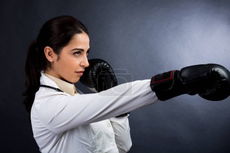 Téléchargez les photos : Médecin femme en manteau blanc et gants de boxe et prête pour la confrontation et la bataille, isolée sur fond blanc - en image libre de droit