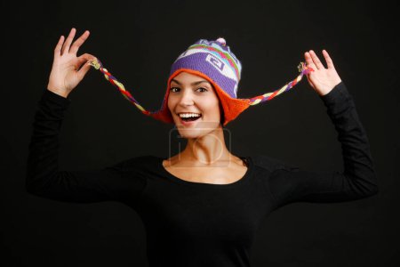 Photo for Beautiful girl with black sweater plays with her colorful Peruvian hat, isolated on black background - Royalty Free Image