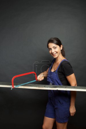 Foto de Hermosa chica con una sierra de trabajo corta una tabla de madera, aislada sobre un fondo negro - Imagen libre de derechos