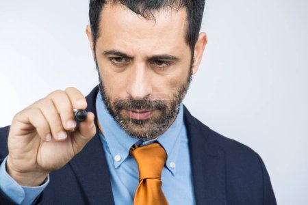 Téléchargez les photos : Homme aux cheveux foncés avec barbe, vêtu d'un costume chemise, veste orange et cravate, dessine avec un marqueur sur une surface transparente hypothétique, isolé sur un fond blanc - en image libre de droit