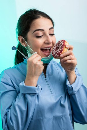 Photo for Dentist, torn between eating a sweet or taking care of her teeth, isolated on a light background - Royalty Free Image