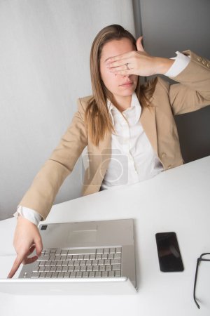 Téléchargez les photos : Femme gestionnaire, assise sur la chaise de travail, apporte une main à son visage afin de ne pas être en mesure de voir tout en pointant son doigt vers le moniteur de son ordinateur pour choisir quelque chose. - en image libre de droit