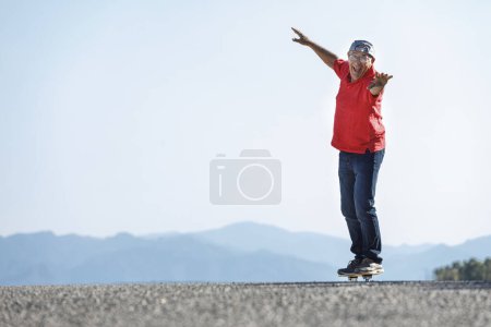 Foto de Senior en jersey rojo disfruta del skateboarding en una carretera rural - Imagen libre de derechos
