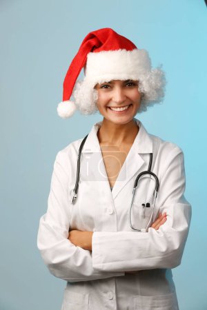 Téléchargez les photos : Belle femme médecin avec manteau blanc et santa claus chapeau isolé sur fond bleu clair tout en offrant un cadeau - en image libre de droit