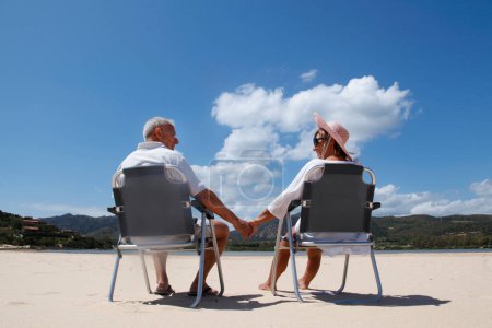 Téléchargez les photos : Heureux couple mature assis sur des chaises longues par la mer - en image libre de droit