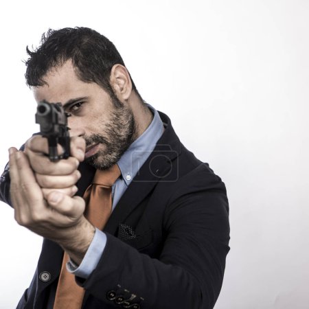 Photo for Dark-haired man with beard dressed in suit with orange jacket and tie points a blank gun - Royalty Free Image
