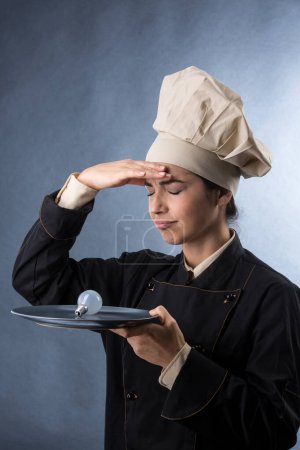 Foto de Chef mujer en uniforme de chef tiene una bombilla en la mano para significar la búsqueda de una buena idea para una receta creativa, aislado en el fondo de luz - Imagen libre de derechos