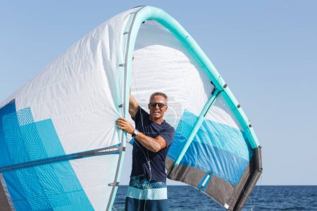 Téléchargez les photos : Homme avec des lunettes de soleil exercices à la plage avec voile de kitesurf - en image libre de droit