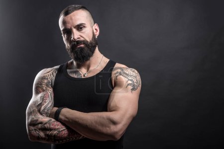 Portrait of handsome strong bearded man with tattoos on dark background