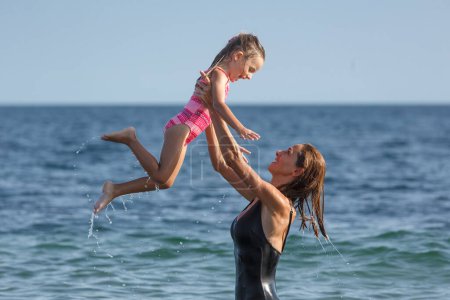 Photo for Mom and daughter in bathing suits play and have fun while swimming in the sea - Royalty Free Image