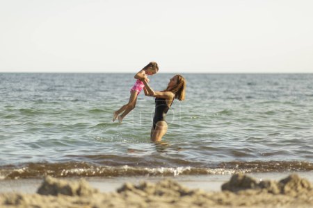Photo for Mom and daughter in bathing suits play and have fun while swimming in the sea - Royalty Free Image