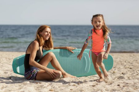 Téléchargez les photos : Mère en maillot de bain avec sa fille s'amuser sur une plage au bord de la mer. - en image libre de droit