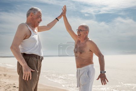 Foto de Feliz pareja de ancianos saludando las manos mientras está de pie en la playa - Imagen libre de derechos