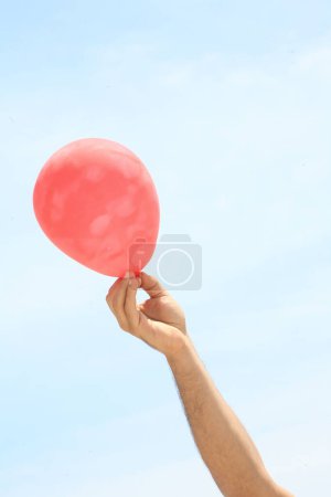 Photo for Hand of a young man holding a colorful balloon on a blue sky background. - Royalty Free Image
