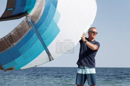 Téléchargez les photos : Homme avec des lunettes de soleil exercices à la plage avec voile de kitesurf - en image libre de droit