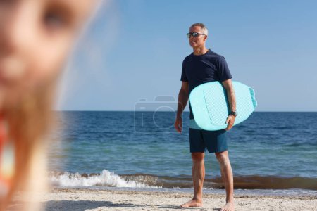 Téléchargez les photos : Homme avec planche de surf à la plage regarde au loin - en image libre de droit
