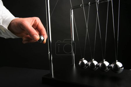 Photo for Newton cradle pendulums steel kinetic balls hand pulling one - Royalty Free Image