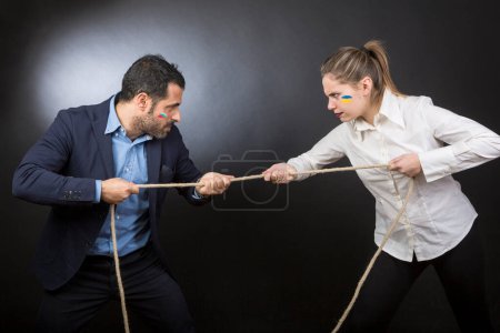 Photo for Man in jacket does the tug of war against a blonde woman. Each of them strives to win over the other. Isolated on a black background - Royalty Free Image