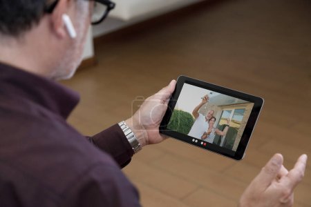 Photo for Tablet held in the hand of a man, on whose screen a couple remotely in videoconference who have just bought a house and show the keys - Royalty Free Image