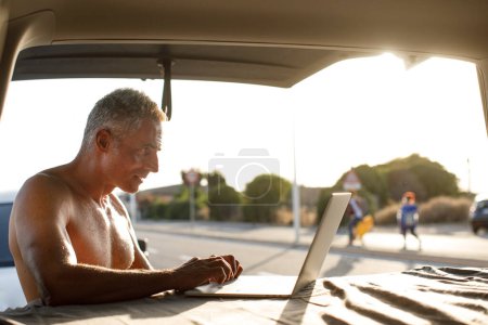 Téléchargez les photos : Un homme torse nu en vacances travaille sur l'ordinateur dans le capot de sa camionnette - en image libre de droit