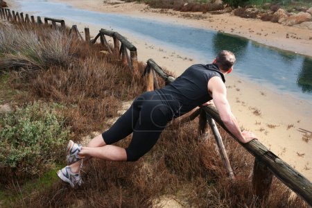 Téléchargez les photos : Homme en vêtements de sport faisant de l'exercice sur la plage - en image libre de droit