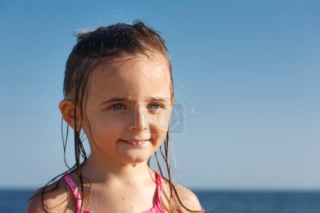 Foto de Niña rubia con los ojos verdes con el pelo mojado se ve feliz, suelto en el fondo del cielo azul - Imagen libre de derechos