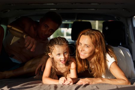 glückliche Familie, bestehend aus Vater, Mutter und Tochter, in Bademode umarmt einander glücklich in dem auf der Straße geparkten Lieferwagen