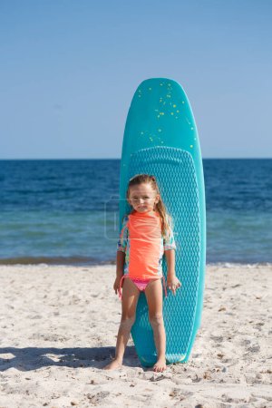 Téléchargez les photos : Petite fille blanche en maillot de bain devant une planche de kitesurf - en image libre de droit